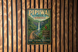 A vintage-style metal sign for the Pipiwai Trail in Hawaii, featuring a waterfall and lush greenery, is displayed on a wooden wall.