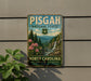 A vintage-style metal sign for Pisgah National Forest in North Carolina, featuring a scenic landscape with pine trees, a waterfall, and pink flowers.