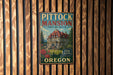 A vintage metal sign for Pitock Mansion in Portland, Oregon, featuring a large illustration of the mansion and surrounded by trees.