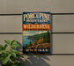 A vintage-style sign for Porcupine Mountain State Park in Michigan, featuring a scenic landscape with mountains, forests, and a lake.