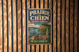 A vintage metal sign with the text "Prairie du Chien Heritage Landscape Wisconsin" displayed on a wooden wall.