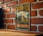 A vintage-style metal sign with a colorful illustration of a pyramid and a dragon, mounted on a brick wall.