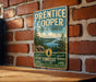 A vintage metal sign for the Prentice Cooper State Forest in Tennessee, featuring a scenic landscape with pine trees and a river.