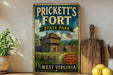 A vintage-style sign for Prickett's Fort State Park in West Virginia, featuring a wooden cabin and a flag, is displayed on a shelf next to a wooden cutting board and some lemons.