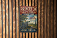 A vintage metal sign for Princeton Battlefield State Park, featuring a cannon and a scenic landscape, is displayed on a wooden wall.