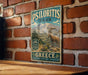 A vintage-style metal sign for PSILORITIS PARK in Greece, featuring a mountain landscape and a goat.