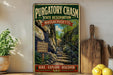 A vintage-style metal sign for Purgatory Chasm State Reserve in Massachusetts, featuring a scenic image of a rocky trail leading up to a waterfall.