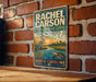 A vintage-style metal sign for Rachel Carson Estuarine Reserve in North Carolina, featuring illustrations of birds and a turtle.