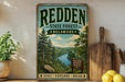 A vintage-style sign for the Redden State Forest in Delaware, featuring a scenic image of a forest and a river.