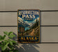 A vintage metal sign for the Resurrection Pass Trail in Alaska, featuring a scenic mountain landscape with a trail leading through it.