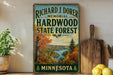 A vintage-style sign for the Richard J. Domer Memorial Hardwood State Forest in Minnesota, featuring a scenic landscape with a river and autumn foliage.