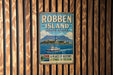 A vintage metal sign for Robben Island, South Africa, featuring a lighthouse and a boat on the water.