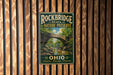 A vintage metal sign for Rockbridge State Nature Preserve, featuring a scenic image of a stone bridge surrounded by lush greenery.