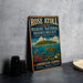 A vintage-style metal sign for Rose Atoll Marine National Monument, featuring an illustration of a tropical island and marine life, is displayed on a gray countertop next to a stack of black camera lenses.