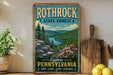 A vintage-style poster advertising Rothrock State Forest in Pennsylvania, featuring a scenic landscape with pine trees, a river, and mountains.