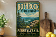 A vintage-style metal sign for Rothrock State Forest in Pennsylvania, featuring a scenic mountain landscape with pine trees and a river.