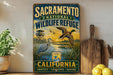 A vintage-style sign for the Sacramento National Wildlife Refuge in California, featuring an illustration of a bird and a duck in a natural setting.