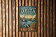 A vintage-style metal sign for the Delta National Heritage Area in Sacramento, California, featuring illustrations of a river, boats, and a bird.