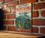 A vintage-style metal sign for the Sacred Island of Okinawa, Japan, featuring an illustration of a traditional Japanese torii gate and a mountainous island landscape.