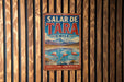 A vintage metal sign with the text "Salar de TARA CHILE" and an illustration of a flamingo in a lake, mounted on a wooden wall.