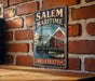 A vintage metal sign for Salem Maritime National Historic Site in Massachusetts, featuring a ship and a building, is displayed on a brick wall.