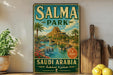 A vintage-style metal sign for Salma Park in Saudi Arabia, featuring a scenic landscape with palm trees, waterfalls, and a castle-like structure.