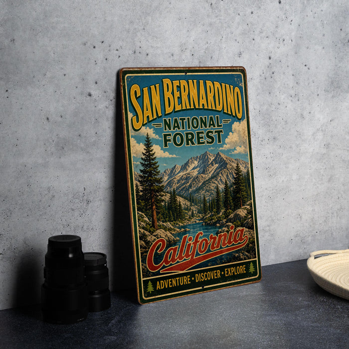 A vintage-style metal sign for the San Bernardino National Forest in California, featuring a scenic mountain landscape and the text "SAN BERNARDINO NATIONAL FOREST CALIFORNIA ADVENTURE - DISCOVER - EXPLORE".