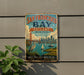 A vintage-style metal sign for San Francisco Bay Estuary, featuring a cityscape, a bridge, and a bird, mounted on a wall.