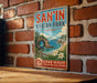 A vintage metal sign for San'In Kaigan Park in Japan, featuring a scenic landscape with a rocky arch, ocean, and flowers.
