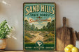 A vintage-style metal sign for the Sand Hills State Forest in South Carolina, featuring a scenic illustration of a forest road surrounded by pine trees and a blue sky.