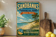 A vintage-style sign for Sandbanks Provincial Park, Ontario, Canada, featuring a beach scene with a sailboat and a pine tree.