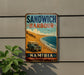 A vintage-style metal sign advertising "Sandwich Harbour Namibia" is displayed on a wall, featuring a vintage car and a beach scene.