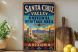 A vintage-style sign for Santa Cruz Valley National Heritage Area in Arizona, featuring a desert landscape with mountains, cacti, and a bell tower.