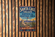 A vintage-style metal sign for Santa Cruz Valley National Heritage Area in Arizona, featuring a desert landscape with mountains, cacti, and a bell tower.