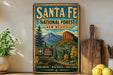A vintage-style metal sign for Santa Fe National Forest in New Mexico, featuring a scenic mountain landscape and the U.S. Forest Service logo.
