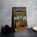 A vintage-style metal sign for "SANTIAGO de COMPOSTELA CIUDAD VIEGIA" is displayed on a table, with a plate and a camera in the background.