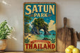 A vintage-style metal sign with the text "SATUN PARK THE HIDDEN PARADISE THAILAND" is displayed on a shelf, accompanied by a potted plant, a wooden cutting board, and some lemons.
