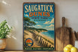 A vintage-style sign for Saugatuck Dunes State Park in Michigan, featuring a scenic beach landscape with a sunset.
