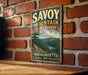 A vintage metal sign for Savoy Mountain State Forest in Massachusetts, featuring a scenic landscape with pine trees, mountains, and a lake.
