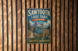 A vintage metal sign for the Sawtooth Lake Trail in Idaho, featuring a scenic mountain landscape and inviting visitors to explore the Sawtooth Mountains.