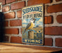 A vintage-style metal sign for the Seedskadee National Wildlife Refuge in Wyoming, featuring a bird perched on a wooden post against a brick wall.