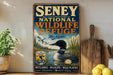 A vintage-style metal sign for Senney National Wildlife Refuge in Michigan, featuring an illustration of a loon and a water loon in a lake surrounded by trees and a water loon.