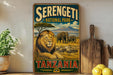 A vintage-style sign for Serengeti National Park in Tanzania, featuring a lion and elephants in a grassy field with a mountain in the background.