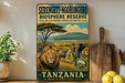 A vintage-style sign for the Serengeti-Ngorongoro Bioshare Reserve in Tanzania, featuring an illustration of a lion and elephants in a grassy savanna landscape with Mount Kilimanjaro in the background.