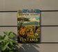 A vintage-style metal sign for the Serengeti-Ngorongoro Biosphere Reserve in Tanzania, featuring an illustration of a lion and elephants in a grassy savanna landscape.
