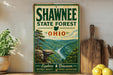 A vintage-style sign for Shawnee State Forest, Ohio, featuring a scenic landscape with a river and mountains.