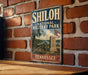 A vintage metal sign for Shiloh National Military Park in Tennessee, featuring a cannon and a monument, mounted on a brick wall.