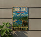 A vintage-style metal sign with the text "SHIRETOKOTO JAPAN" and an illustration of a bear in a natural setting, with mountains in the background.