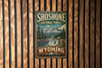 A vintage-style metal sign for Shoshone National Forest in Wyoming, featuring a mountain landscape with a waterfall.