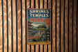 A vintage-style metal sign with the title "SHRINES AND TEMPLES OF NIKKO JAPAN" is displayed on a wooden wall.